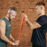 Two men engaging in a resistance band workout in a brick-walled gym setting.